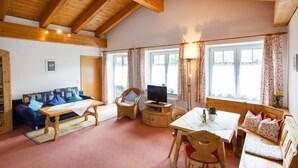 Una sala de estar acogedora con techo de madera, un sofá, una mesa, un televisor y una ventana con cortinas.
