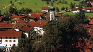 A town with red-roofed buildings, a prominent church with a dome, and mountains in the background. - Zwei-Raum-Ferienwohnung Steinplatte 36qm, Dusche/WC, Extra-Schlafzimmer, Küchenzeile, Balkon (Reit im Winkl)