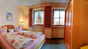 A bedroom with two beds, a wooden wardrobe, and two windows with curtains. - Zwei-Raum-Ferienwohnung Steinplatte 36qm, Dusche/WC, Extra-Schlafzimmer, Küchenzeile, Balkon (Reit im Winkl)