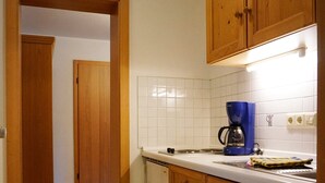 A small kitchen with wooden cabinets, a white countertop, and a blue coffee maker. - Zwei-Raum-Ferienwohnung Steinplatte 36qm, Dusche/WC, Extra-Schlafzimmer, Küchenzeile, Balkon (Reit im Winkl)