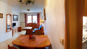 A narrow hallway leading to a dining area with a table and chairs, a kitchen with wooden cabinets, and a door on the right. - Zwei-Raum-Ferienwohnung Steinplatte 36qm, Dusche/WC, Extra-Schlafzimmer, Küchenzeile, Balkon (Reit im Winkl)