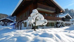 Eine Holzhütte mit geneigtem Dach, umgeben von verschneitem Gelände und Bäumen.