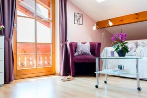 A room with a wooden floor, a purple sofa, a glass coffee table, and a window with curtains. - Zwei-Raum-Ferienwohnung "Panoramablick", 70qm, 2. separate Schlafgelegenheit, 2 Balkone (Reit im Winkl)