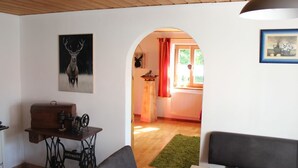 Et værelse med træloft, en symaskine på et bord, et gevir og en døråbning til et andet værelse med en radiator og et vindue med røde gardiner.