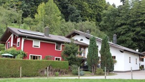 Et rødt og hvidt hus med skråt tag, omgivet af grøn vegetation og træer.