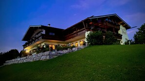 A large, multi-story building with a sloped roof, wooden balconies, and a stone retaining wall. - Vacation apartment Bergfeuer, for 1-4 persons (Berchtesgaden)
