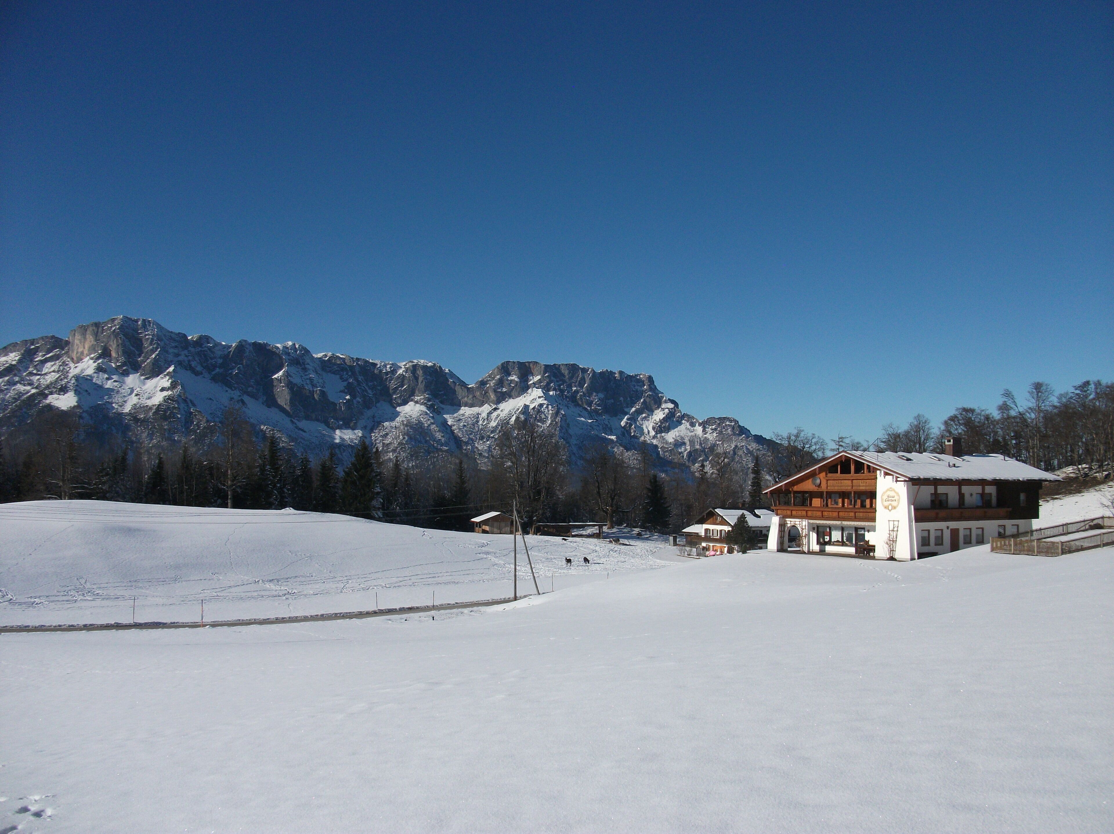 A snow-covered landscape with a mountain range in the background and a building with a wooden facade.