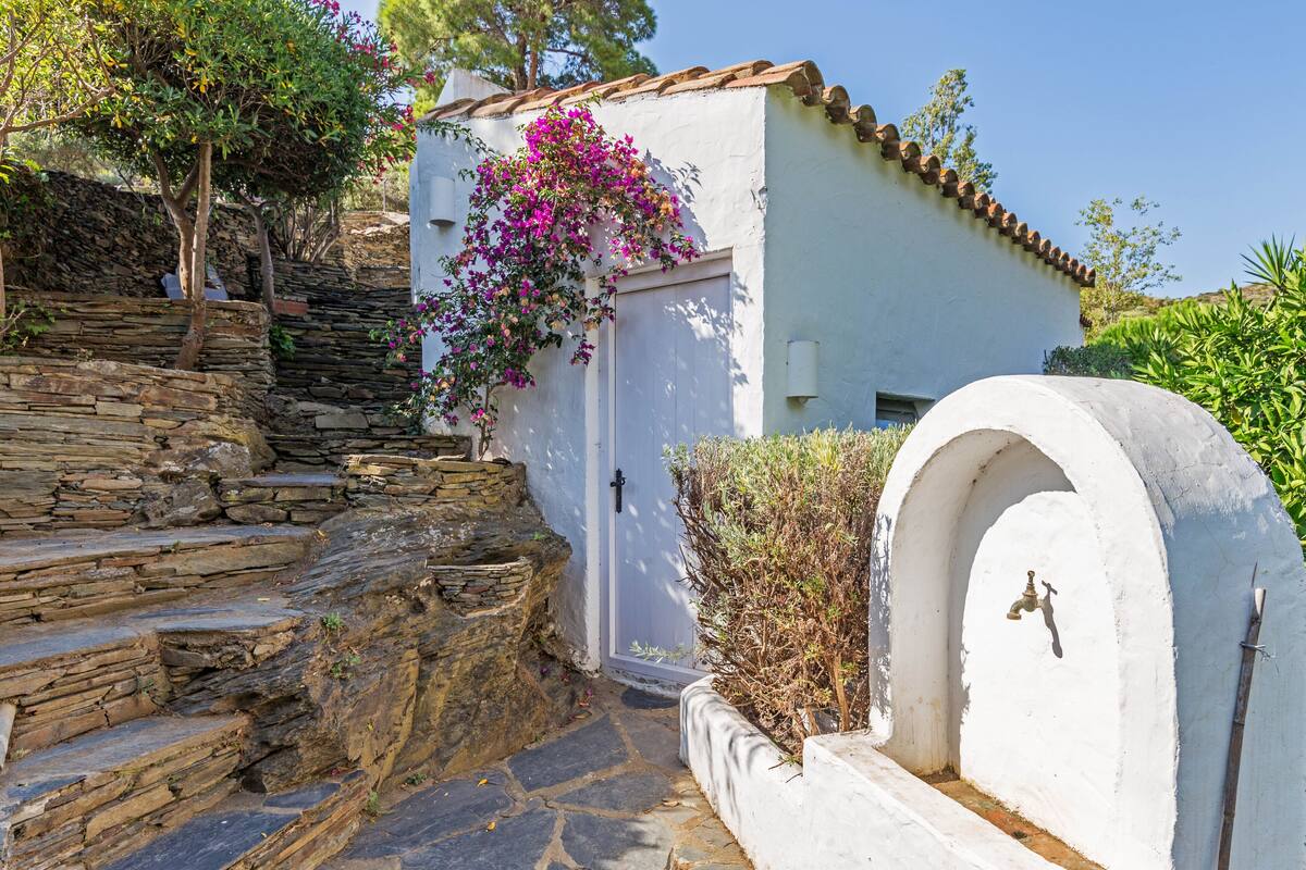 Una escalera de piedra que lleva a un edificio blanco con una puerta y un pequeño arco donde hay un grifo.