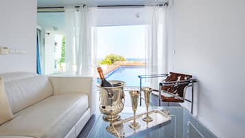 Una sala de estar moderna con un sofá blanco, una mesa de vidrio con cubiertos y vistas a una piscina y vegetación.