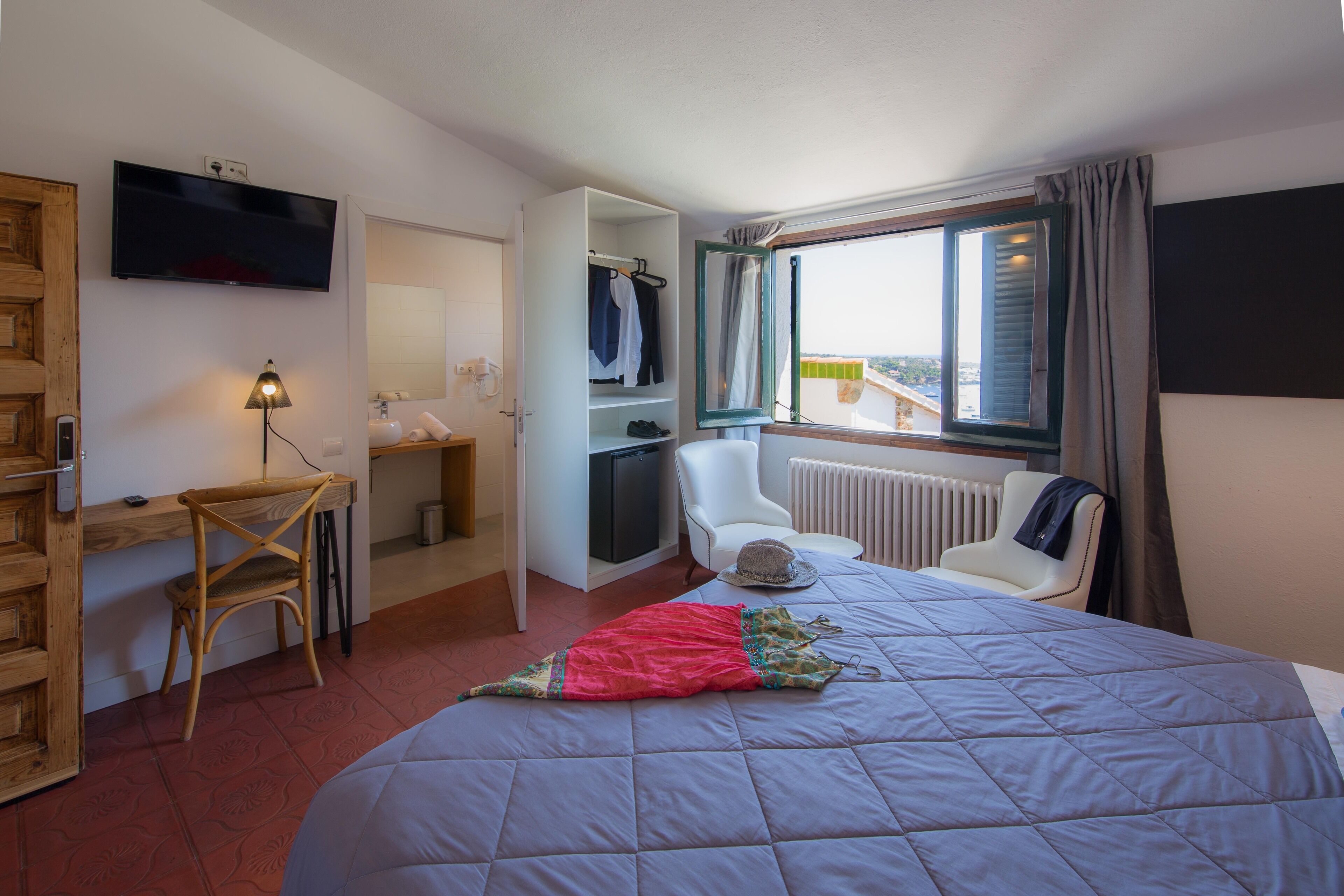 Ein Hotelzimmer mit Bett, Schreibtisch, Stuhl, Fernseher und einem Fenster mit Vorhängen.