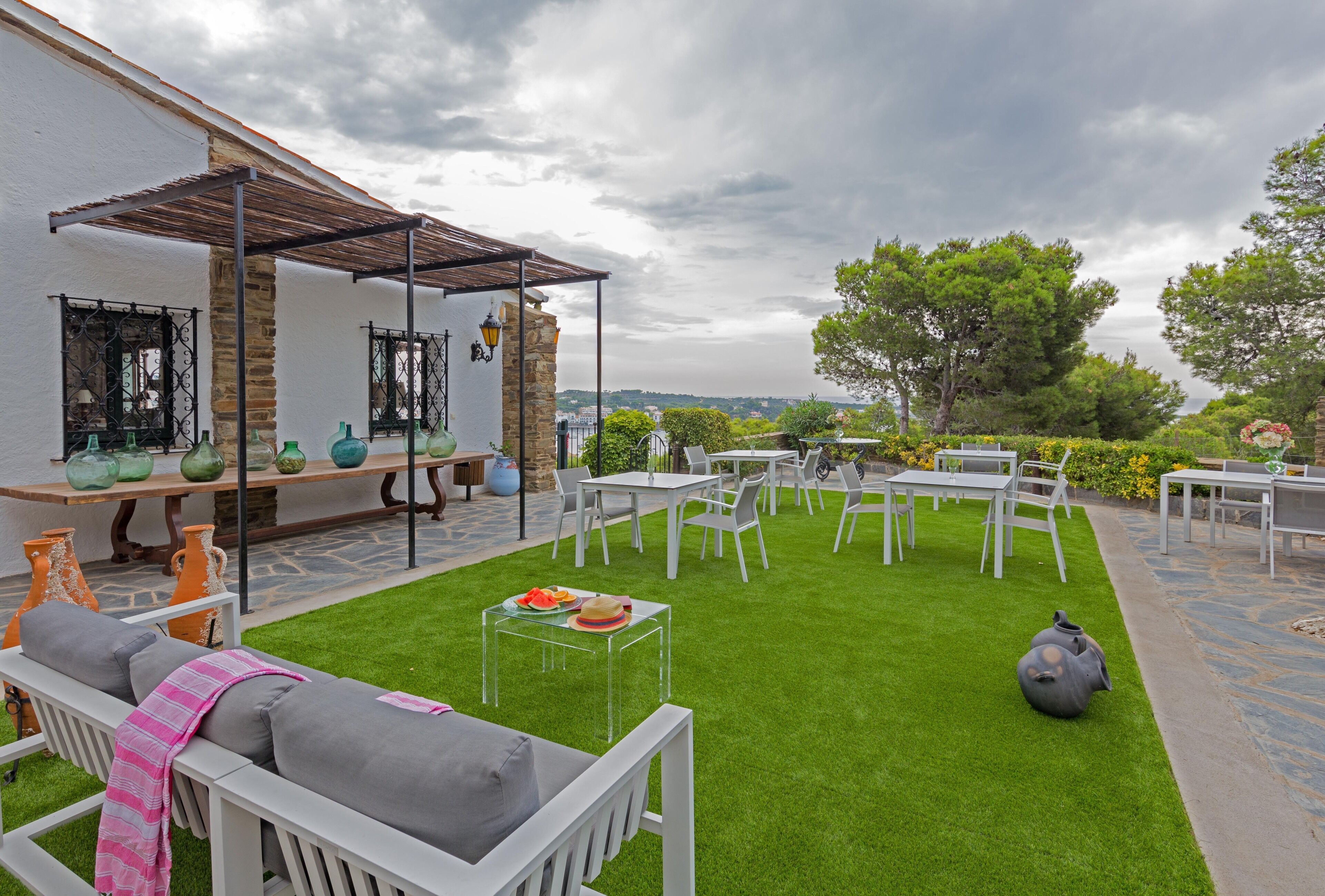 An outdoor patio with white furniture, a clear glass table with food, and a stone wall.