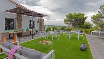 An outdoor patio with white furniture, a clear glass table with food, and a stone wall.