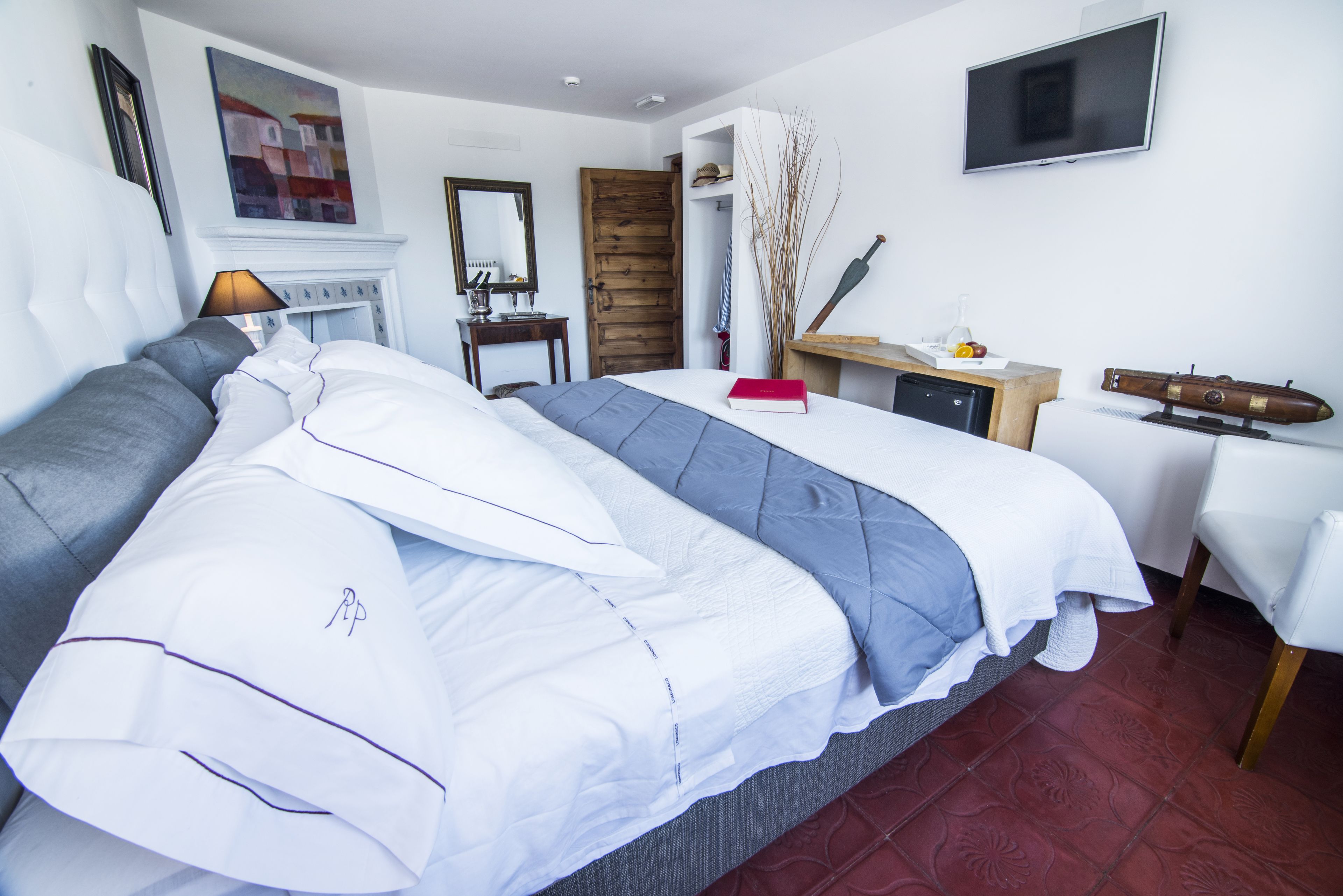 A bedroom with a bed, a desk, a television, a fireplace, and a mirror.