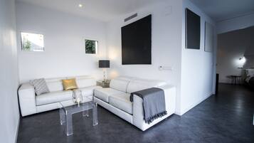 Una sala de estar moderna con un sofá blanco, una mesa de centro de vidrio y una manta gris.