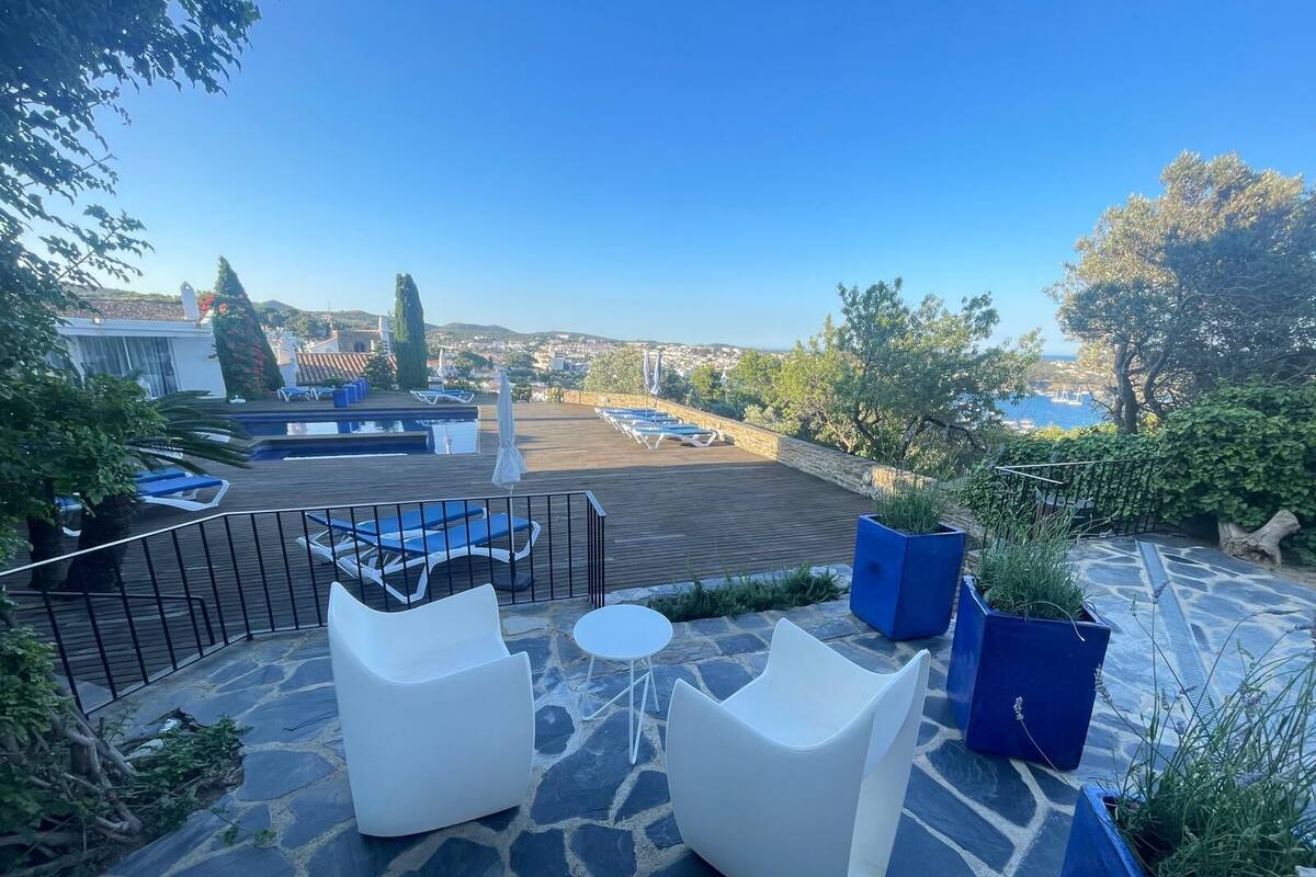 Un patio exterior con sillones blancos, una mesita y macetas azules.