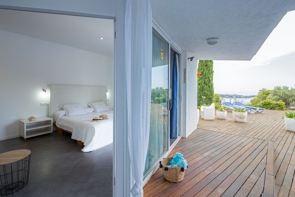 A modern bedroom with a large sliding glass door leading to a wooden deck. - Hotel Rec de Palau (Cadaqués)