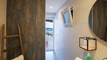 A bathroom with a wooden ladder, two white towels, a mirror, and a small shelf with a bottle.