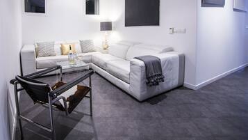 Un salon moderne avec un canapé blanc, une table basse en verre et un fauteuil en cuir.