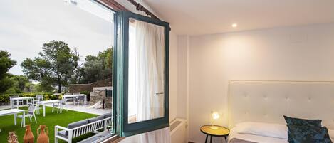 Un dormitorio con una cama grande, vista a un patio exterior con mobiliario y una ventana con cortinas.