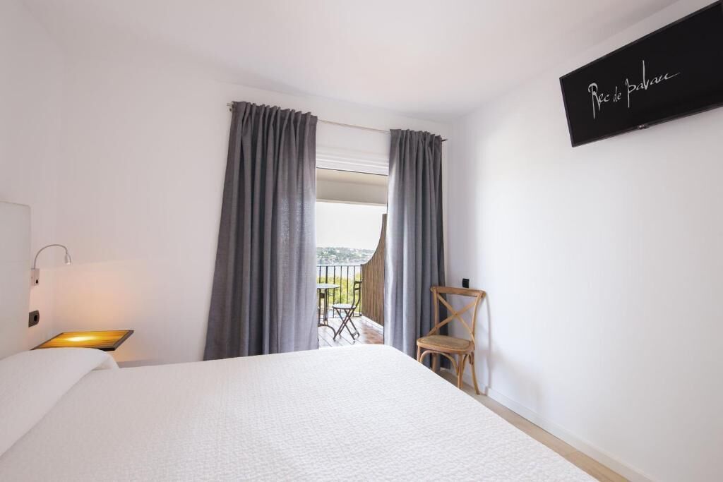 Habitación de hotel con cama, una silla, una mesa y un balcón con vistas.