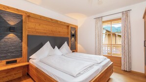 Een houten bed met witte lakens in een kamer met een stenen accentmuur en een raam met gordijnen.