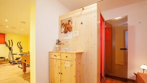 Een houten kast met een bordje, fitnessapparatuur en een rood verlichte deur in een kamer met houten vloeren en witte muren.