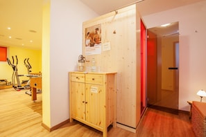 A wooden cabinet with a sign, exercise equipment, and a red-lit door in a room with wooden flooring and white walls.