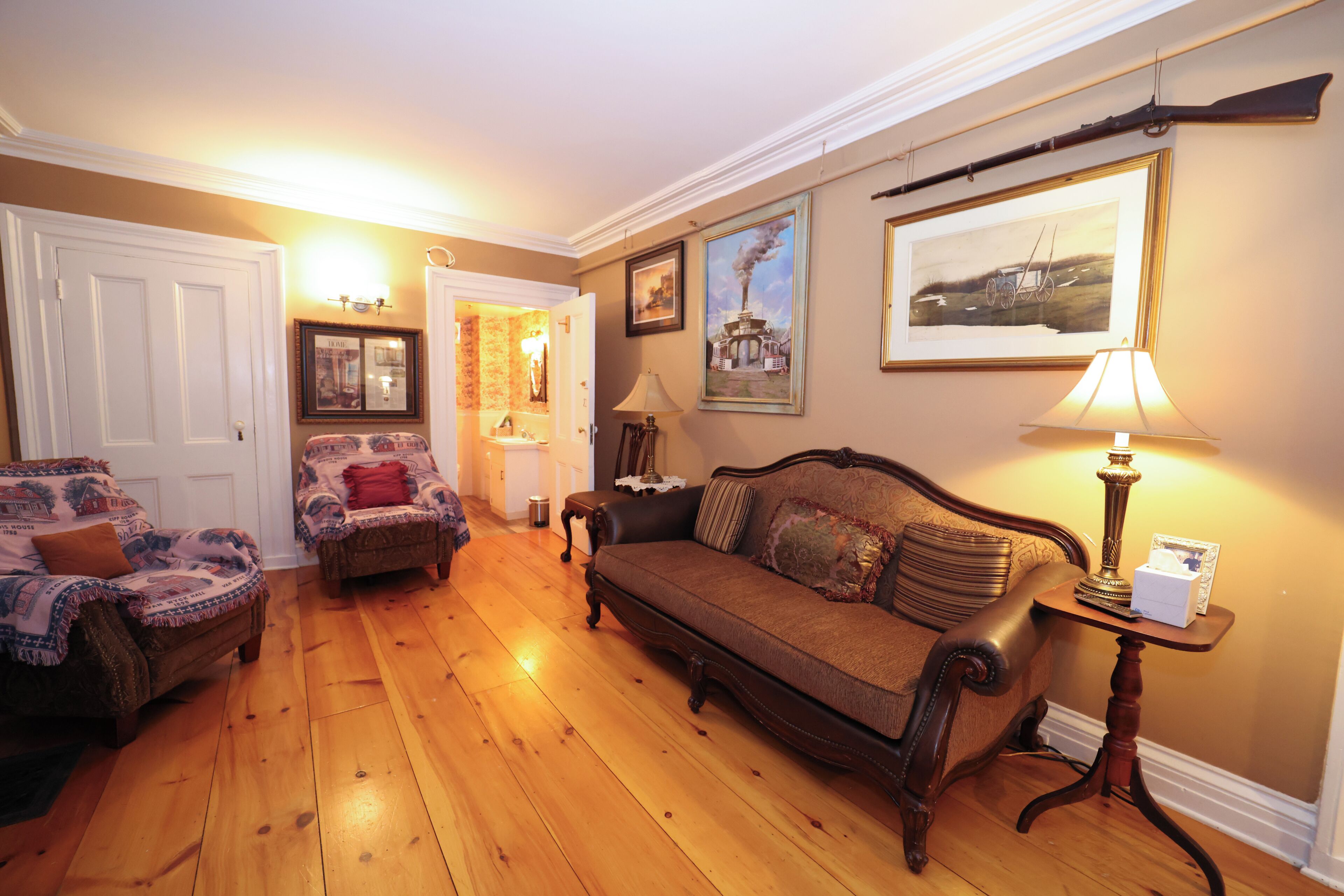 A living room with a wooden floor, two sofas, a table with a lamp, and framed pictures on the wall.