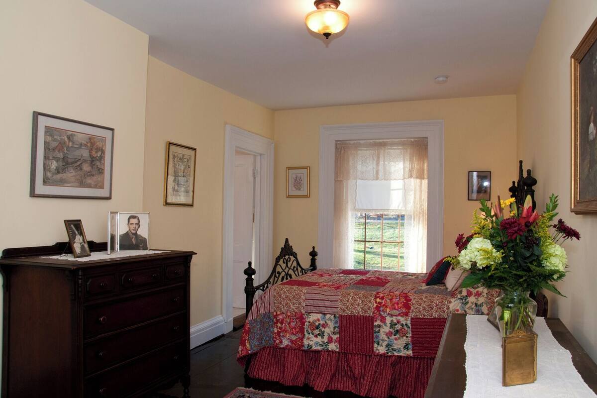 Un dormitorio con cama, cómoda, cuadros enmarcados y una ventana con vistas.