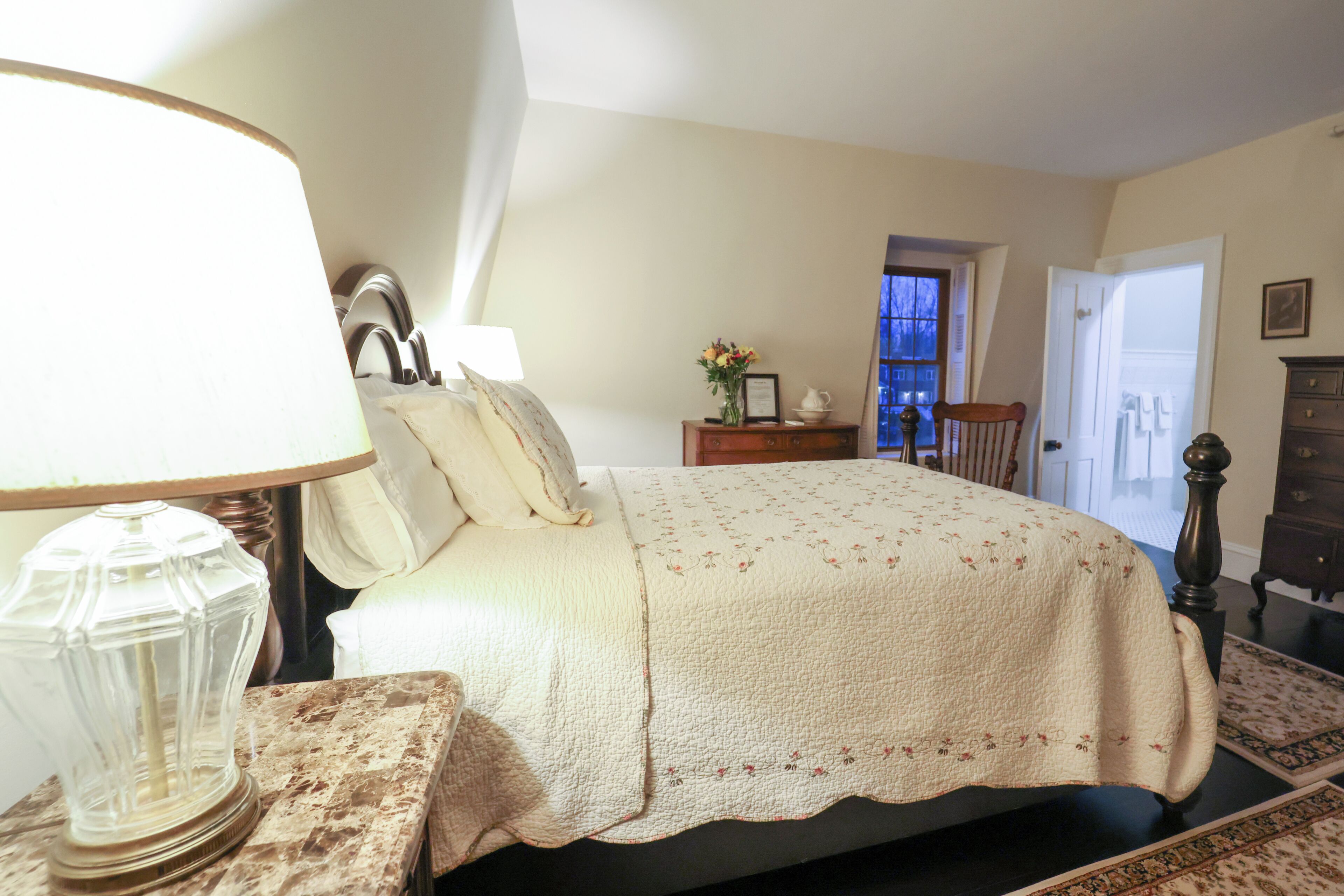 A bedroom with a bed, a nightstand, a lamp, a dresser, and a window.