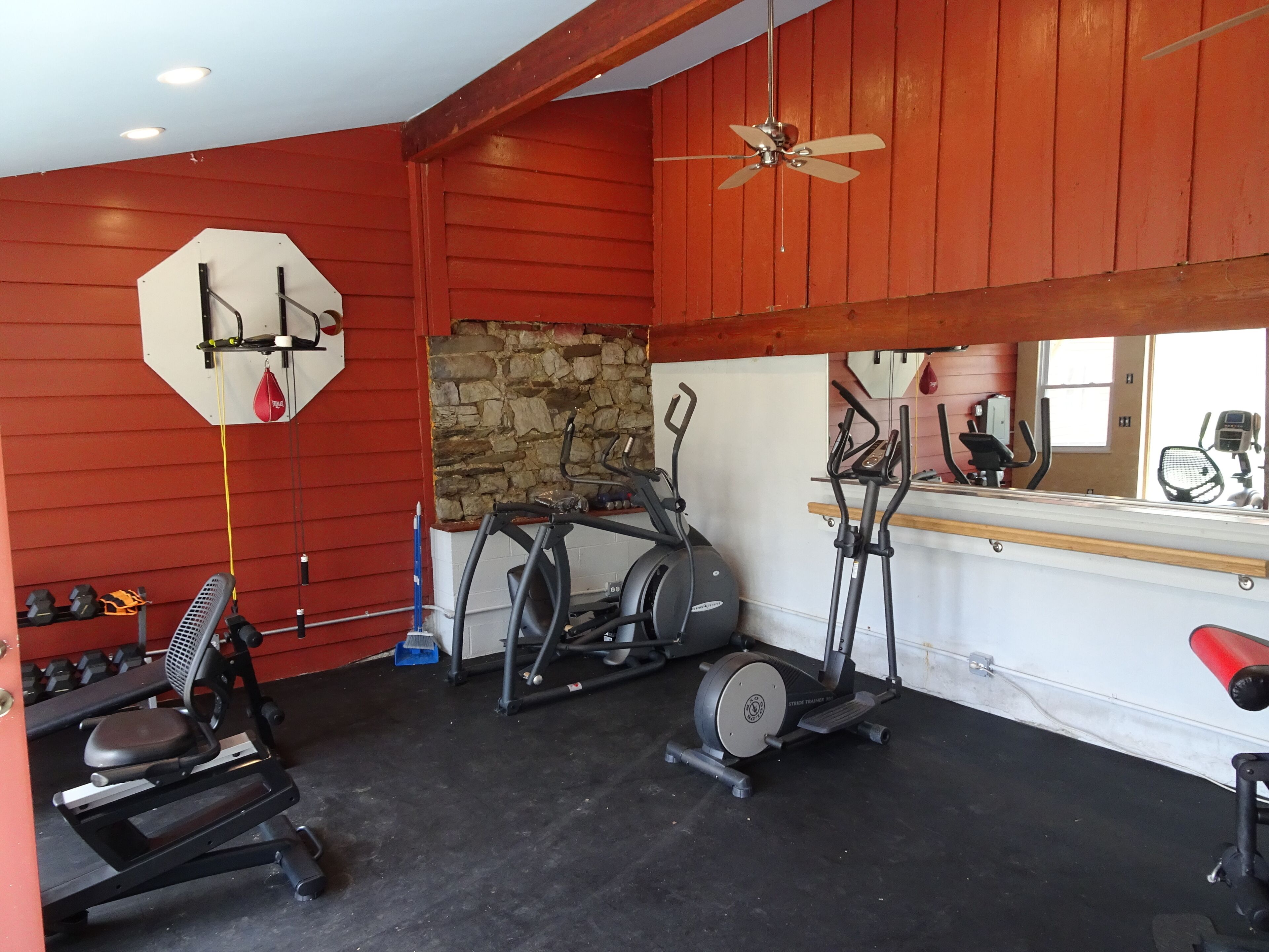 A gym with exercise equipment, a punching bag, and a stone wall.