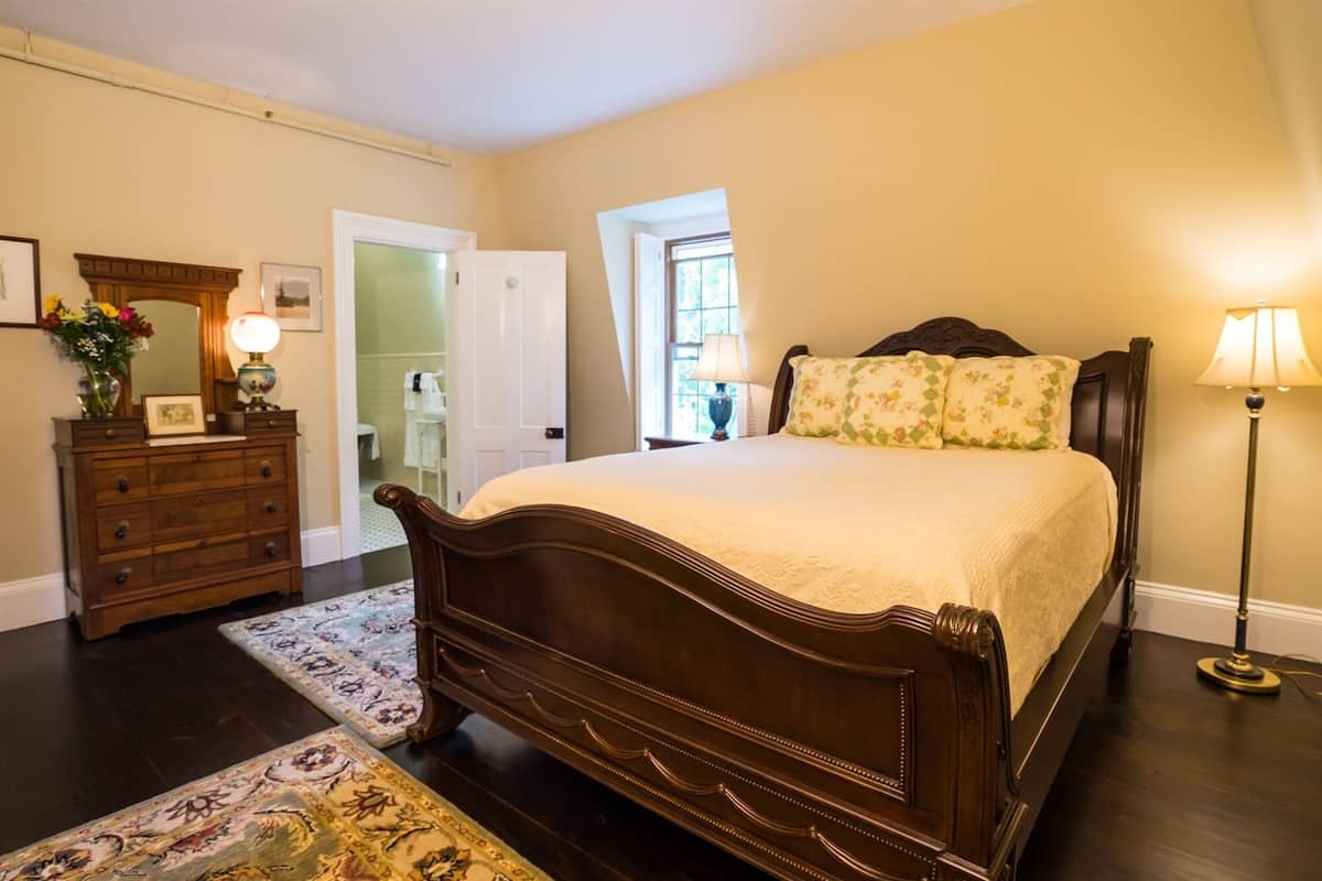Un dormitorio con una cama de madera, un aparador, un espejo y una lámpara.