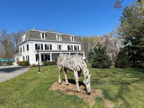 Un grand bâtiment blanc à la façade symétrique, avec une entrée centrale flanquée de colonnes et une statue de cheval en premier plan.