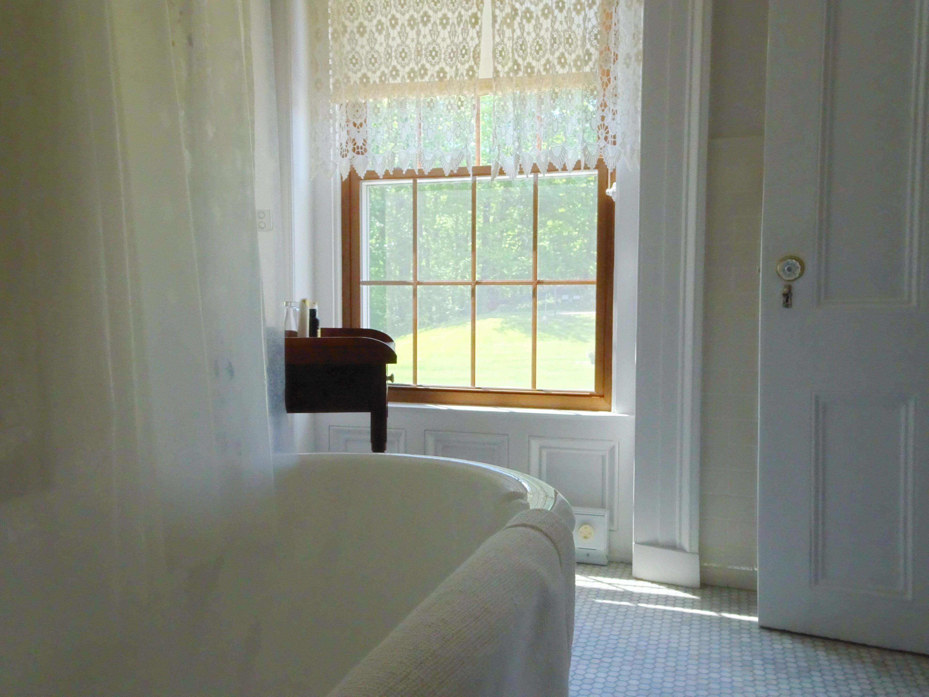 Una habitación con un ventanal grande, una cama, una mesita y una puerta.