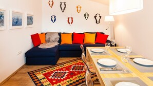 Een moderne woonkamer met een bank, kleurrijke kussens, een eettafel voor vier personen en geweegde antilopehoorns aan de muur.