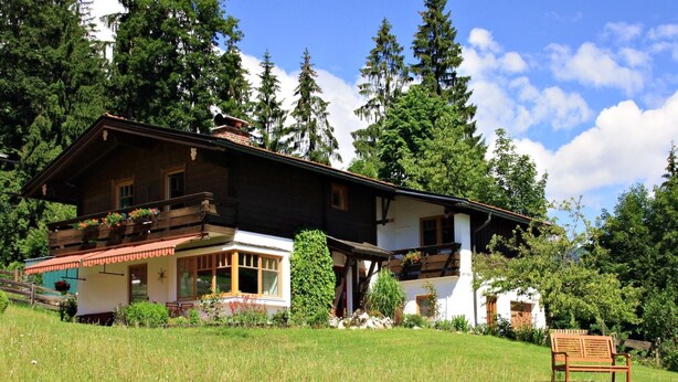 Een klassiek chalet met een houten balkon, een klein portaaltje en een bankje op de voorgrond.