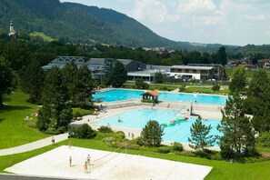 A large outdoor swimming pool surrounded by a grassy area with trees and a building in the background. - Apartment 3 86sqm, balcony, kitchen, 2 bedrooms, living room, max 4 p., WLAN (Ruhpolding)
