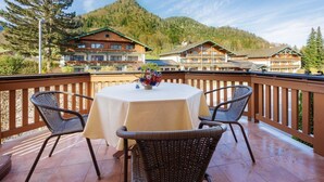 A round table with a white tablecloth and two wicker chairs on a balcony with a wooden railing.