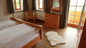 Ein Schlafzimmer mit einem hölzernen Bett, einem Sessel, einem Schminktisch und einem Fenster mit Vorhängen.