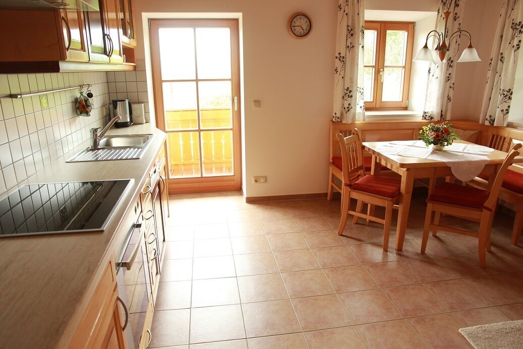 A kitchen with a sink, stove, and window. There is a dining table with chairs and a clock on the wall.