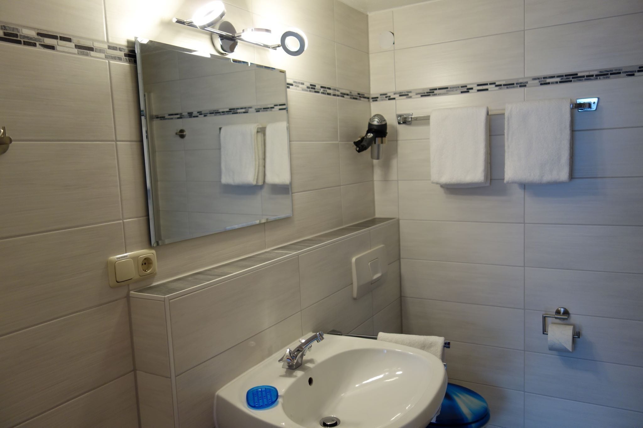 Een badkamer met een wastafel, spiegel, handdoekhouder en douche.