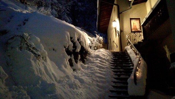 A snow-covered staircase leading to a building with a lit exterior light and a framed picture on the wall. - Vacation apartment no. 1 Watzmann, 70sqm for 2 persons (Berchtesgaden)
