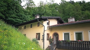A two-story building with a balcony, a staircase, and a garden with yellow flowers. - Vacation apartment no. 1 Watzmann, 70sqm for 2 persons (Berchtesgaden)