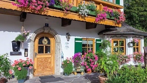 A traditional chalet with a wooden balcony adorned with colorful flowers, a stone entrance, and a small garden area. - holiday flat (Ramsau bei Berchtesgaden)