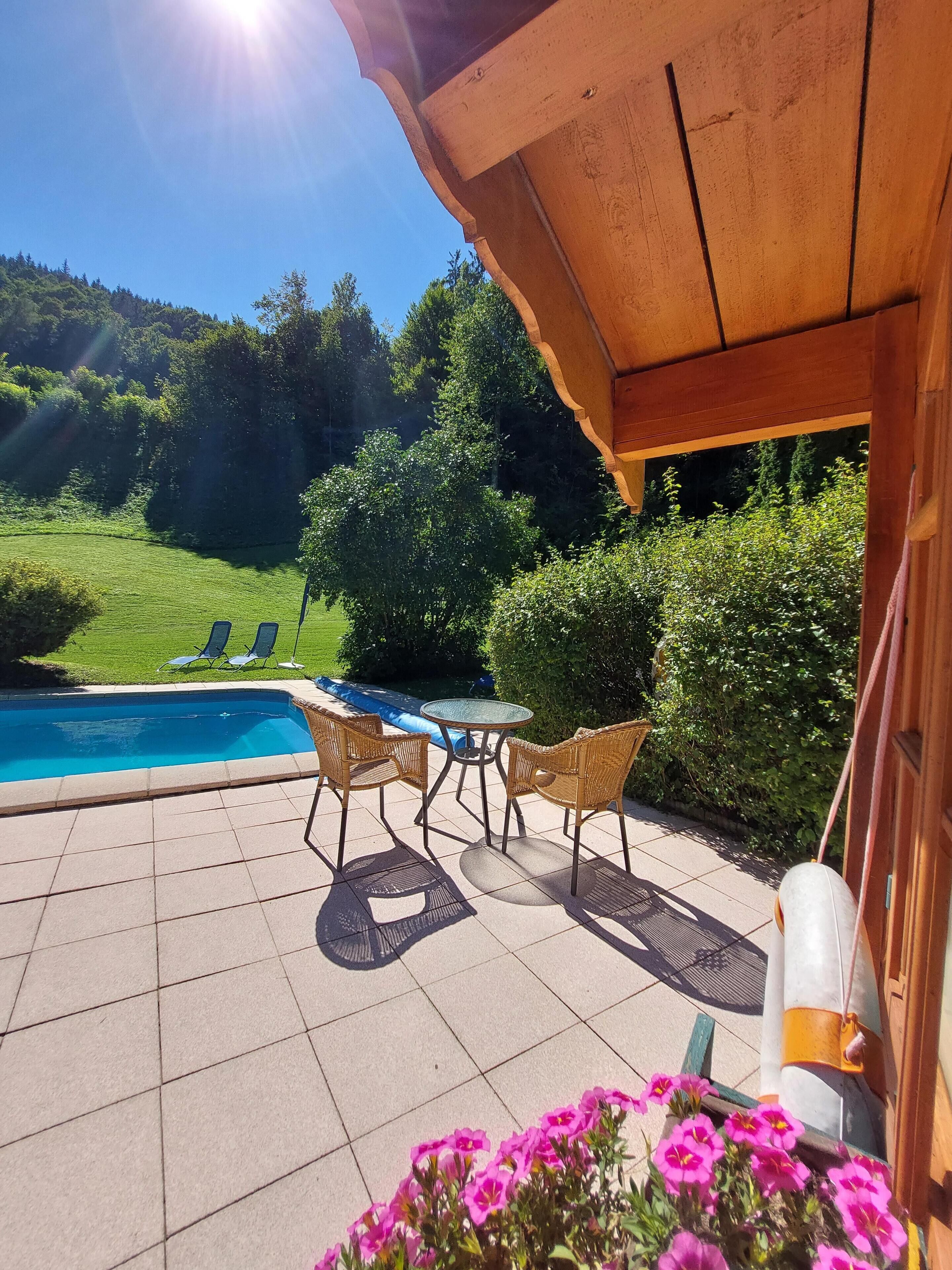 En patio med pool, flet møbler og udsigt over det grønne område.