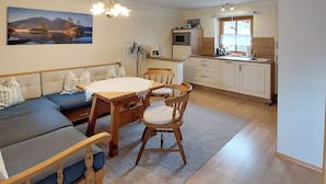 A cozy living room with a sofa, dining table, and chairs, a kitchen area with a window, and a staircase. - holiday flat (Ramsau bei Berchtesgaden)