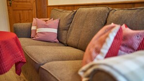 Een bruine bank met een rood-wit geruit kussen en een wit kussen met stippen.