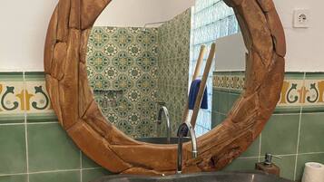 A bathroom with a round wooden-framed mirror, a stone sink, and green patterned tiles.