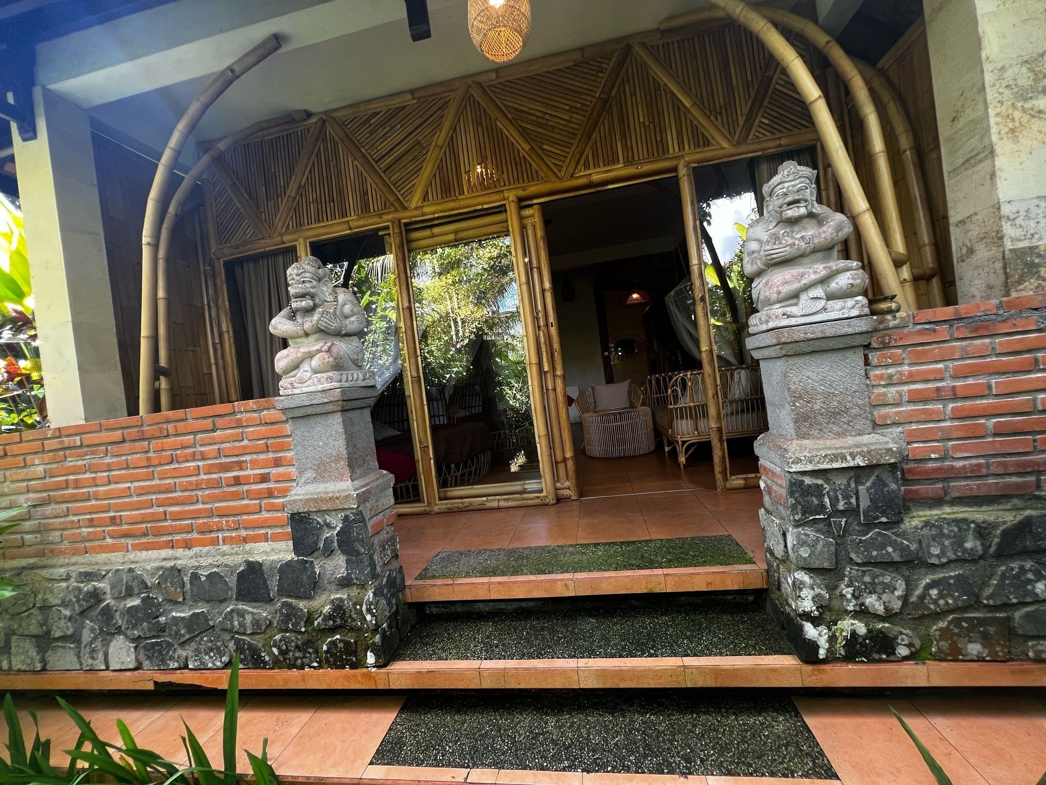 Uma entrada tradicional com pilares de pedra, um arco de bambu e uma porta de vidro que dá para o interior.