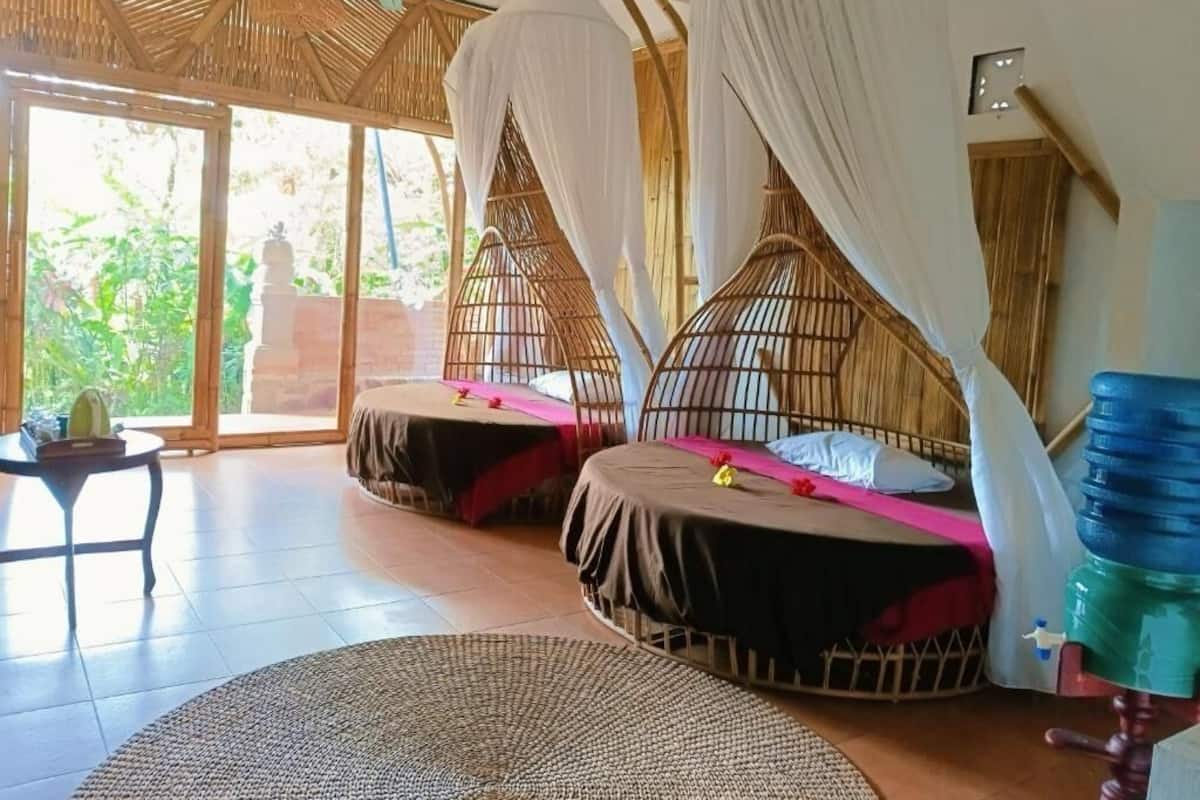 A room with two beds, each with a canopy, a round woven rug, and a table with a chair.